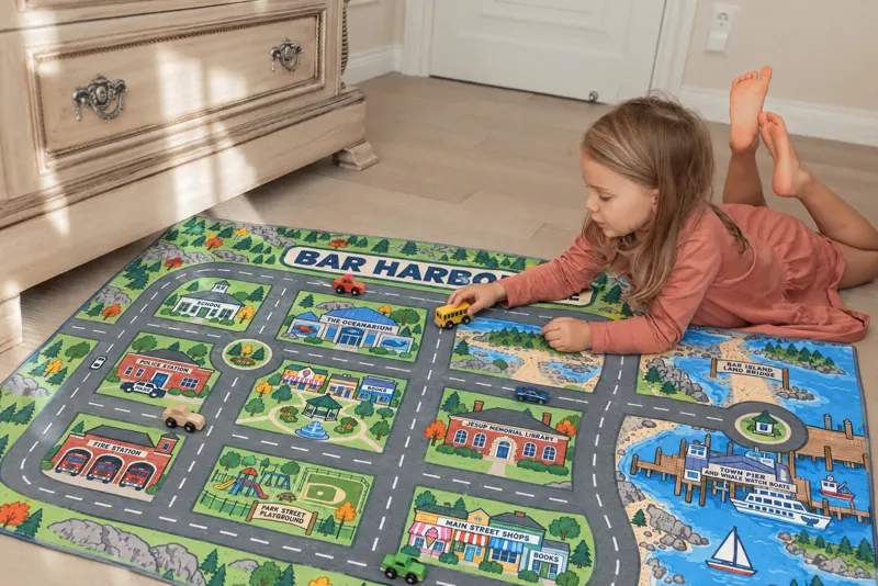A girl lying beside a Bar Harbor rug, pushing a school bus along the harbor road